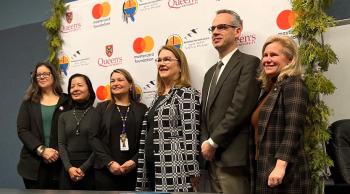Six people line up in front of a banner with logos on it for a photo.