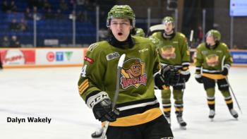 A teen hockey player in a moss green jersey on the ice. He pumps his glove in a celebratory gesture.