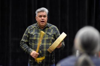 A man stands on a stage using a hand drum and sings.