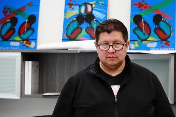 A man stands in front of three colourful abstract paintings. 