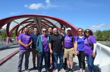 A group of smiling people stand on a bridge over a river for the photo.