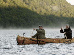 Two First Nations men paddle a birchbark canoe.