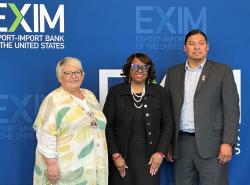 Two woman and one man stand in front of a blue background with the words EXIM printed in the left-hand top corner.
