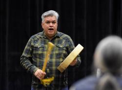 A man stands on a stage using a hand drum and sings.