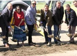 People line up with shovels digging into the ground for a ceremonial sod turning.