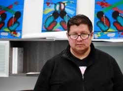 A man stands in front of three colourful abstract paintings. 