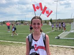 A young tween girl smiles at the camera. She is wearing an Ontario jersey and a headband with two Canadian flags standing upright on it.