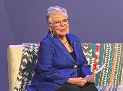 A woman sits on a couch as she speaks.